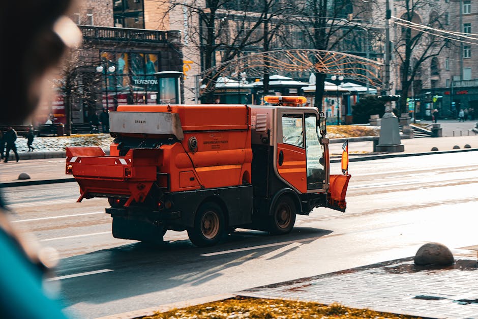 Three professional cleaners from Cleaners Kentish Town dressed in grey shirts and red overalls are standing in a modern living room, each holding a cleaning tool. The first cleaner on the left is holding a vacuum cleaner nozzle, while the center cleaner is holding a handheld vacuum with a cord, and the third cleaner on the right is holding a mop. The room features a polished concrete floor, a black accent wall, and a large window allowing natural light to illuminate the space. Visible cleaning equipment includes a yellow wet-dry vacuum and a blue dustpan with brush, indicating a comprehensive cleaning operation. The scene demonstrates thorough surface cleaning and hygiene maintenance typical of deep cleaning services offered by [COMPANY_NAME], emphasizing high standards of cleanliness in residential environments, aligning with the page about trusted deep cleaning services in Kentish Town.